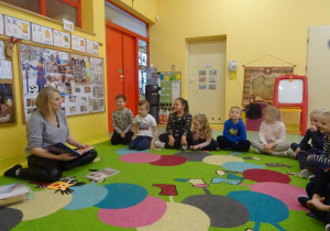 Grupa dzieci siedzi w półkolu wokół pani Magdaleny Siupy dyrektor Miejsko- Gminnej Biblioteki w Kleczewie, która czyta bajkę "O wilku, który nie lubił świąt"